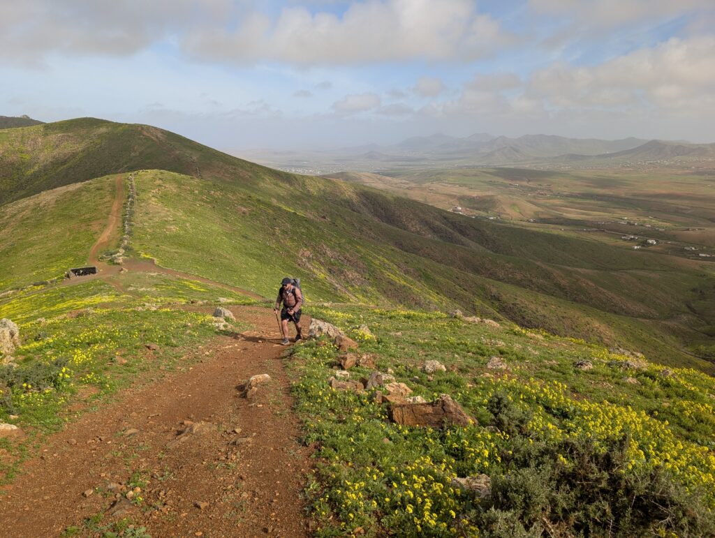 Aufstieg zum Morro del Cortijo, dem höchsten Punkt des GR 131 auf Fuerteventura, ein Trail Shelter im Hintergrund